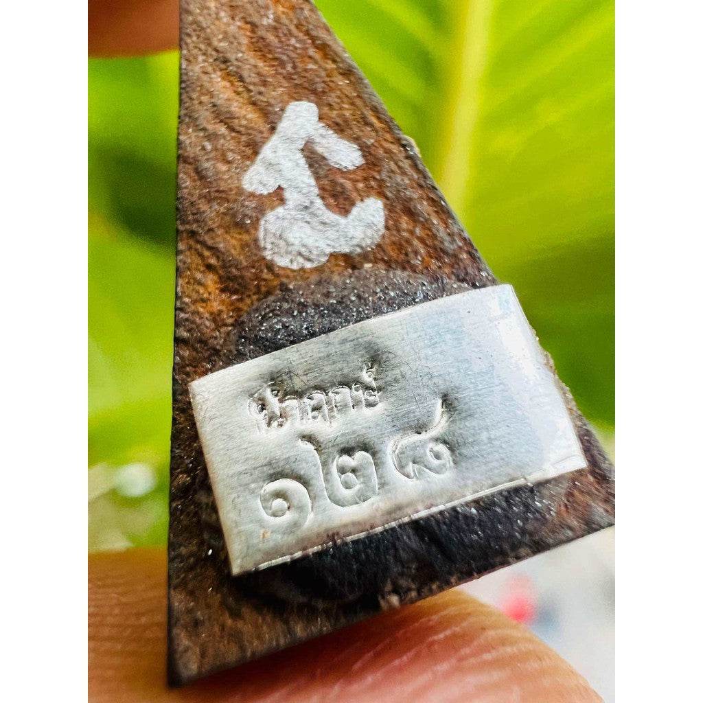 Close up of triangular wooden amulet with silver nameplate and painted symbol Ancient Plal Tai amulet for spiritual protection.