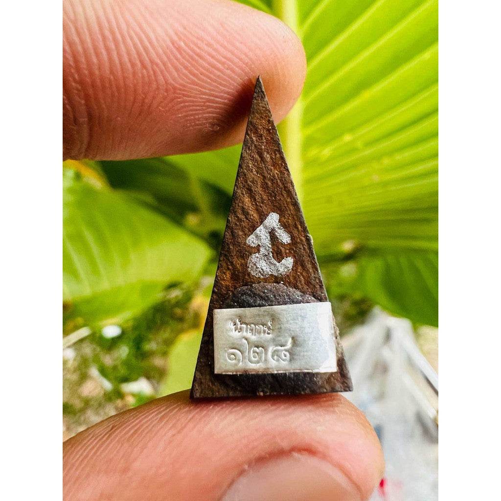 Ancient Plal Tai amulet for spiritual protection. Small triangular wooden amulet with silver plaque held between fingers