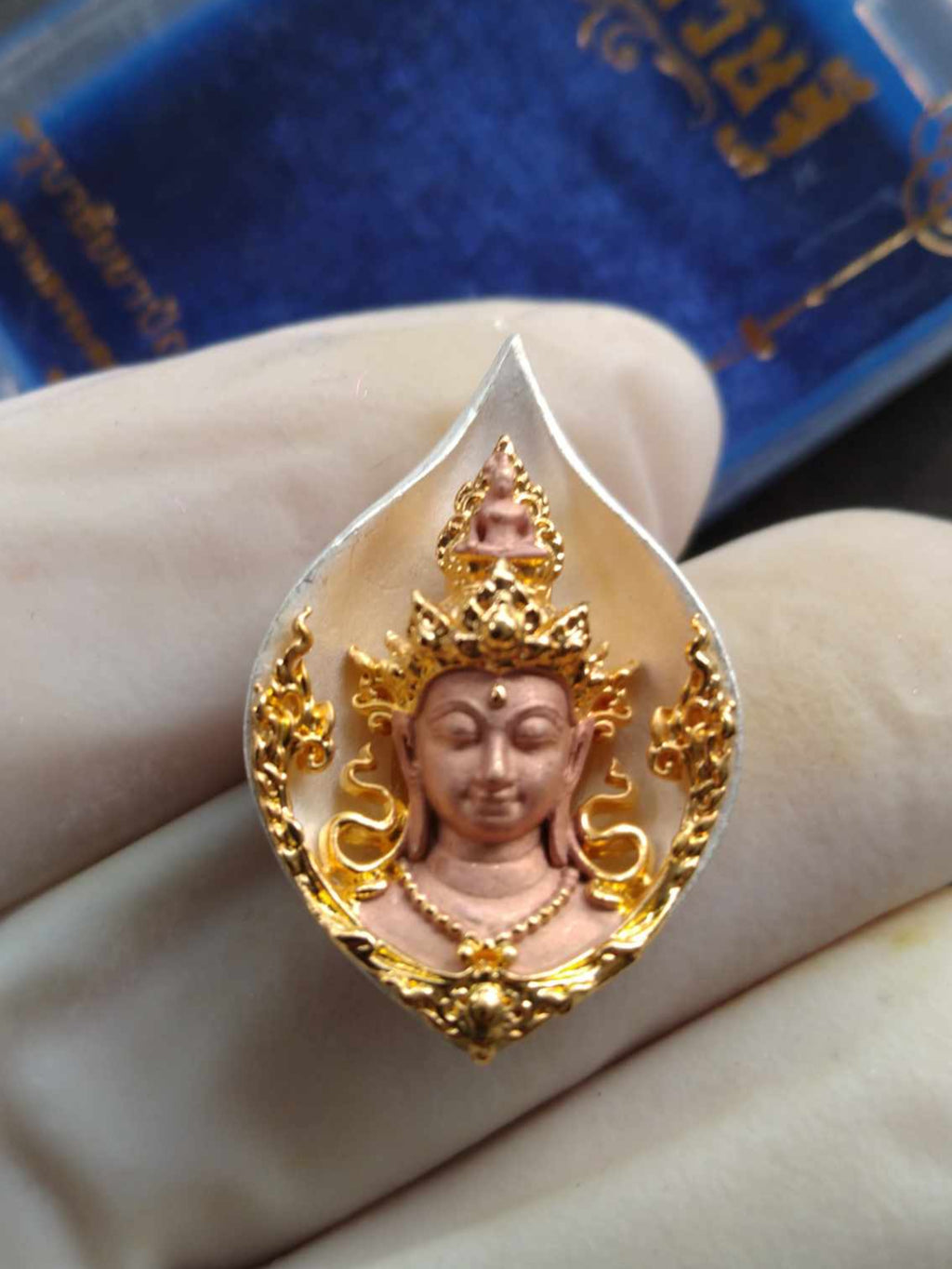 Avalokiteshvara Bodhisattva amulet Thai gold and copper carved deity pendant in ornate bezel shown in gloved hand
