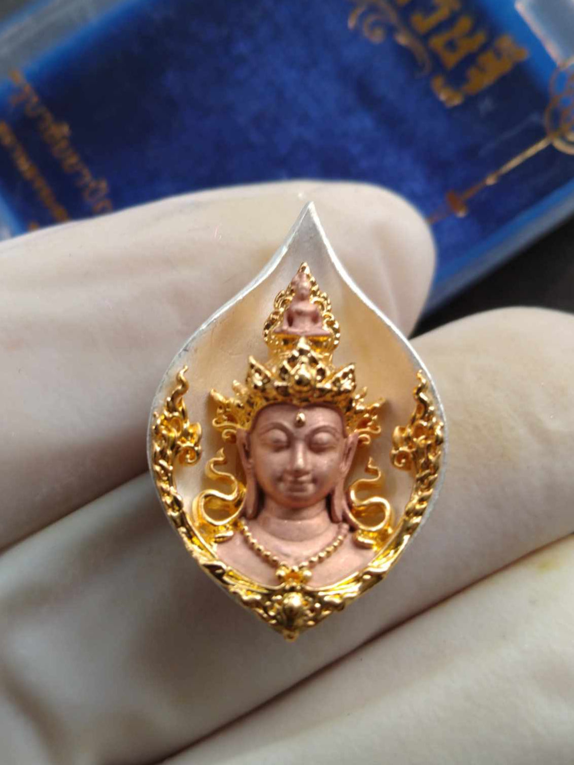 Avalokiteshvara Bodhisattva amulet Thai gold and copper carved deity pendant in ornate bezel shown in gloved hand