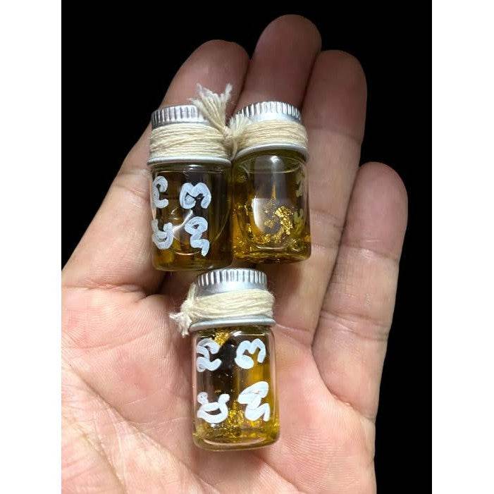 Hand holding three small Thai blessing vials with gold flakes and white script buy Thai spiritual charm for romance