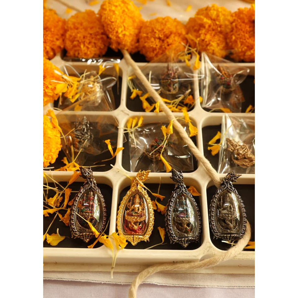Thai amulet for success and prosperity displayed with vibrant marigold flowers and decorative packaging