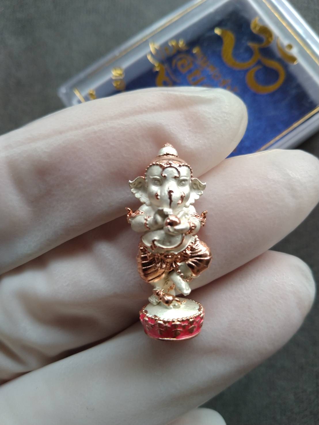 Thai Blessing Co Ganesh Noi amulet Thailand small gold and silver Ganesha pendant with red base held in gloved hand