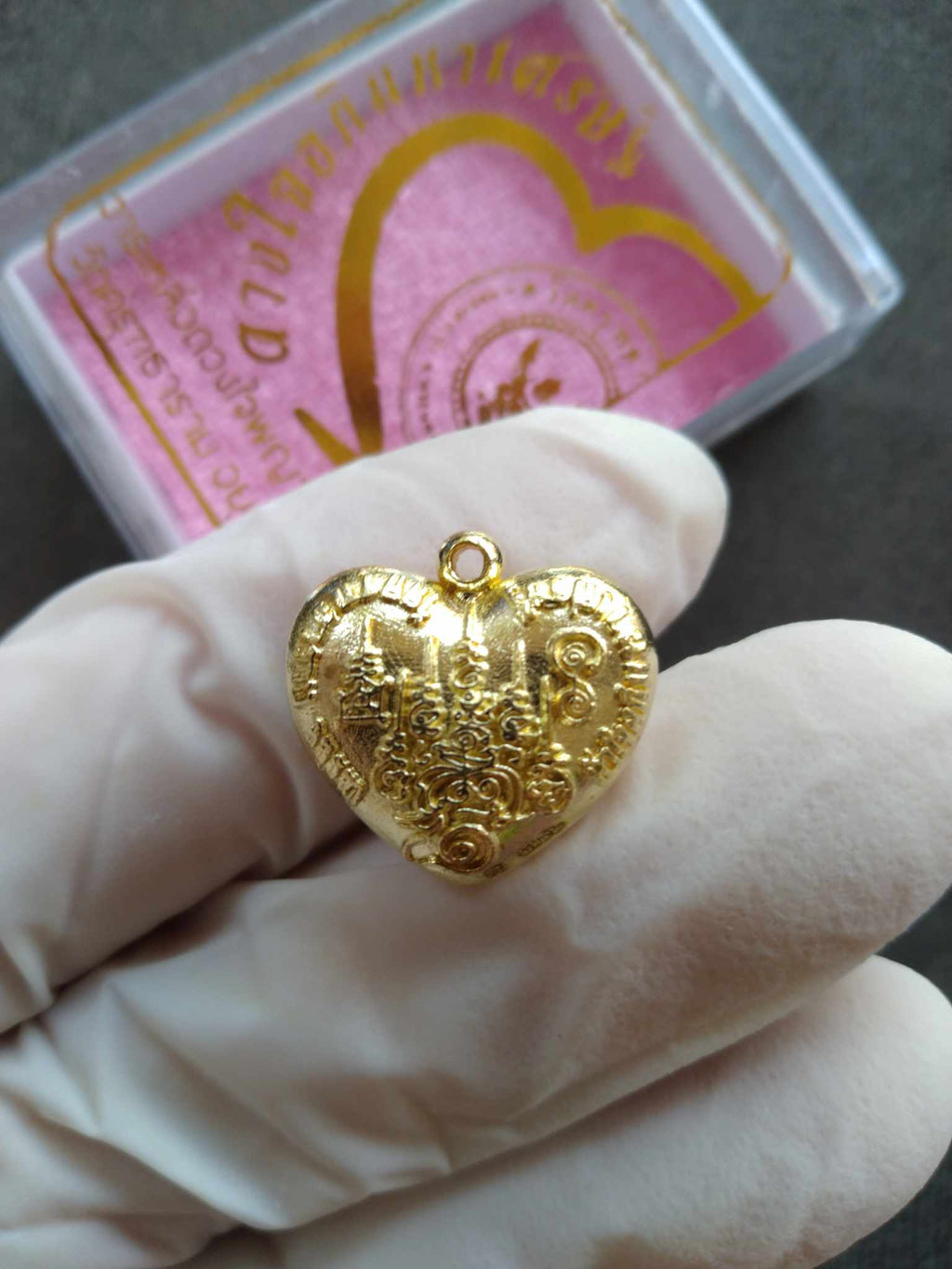 Garuda heart amulet gold heart pendant with intricate Garuda engraving held in gloved hand