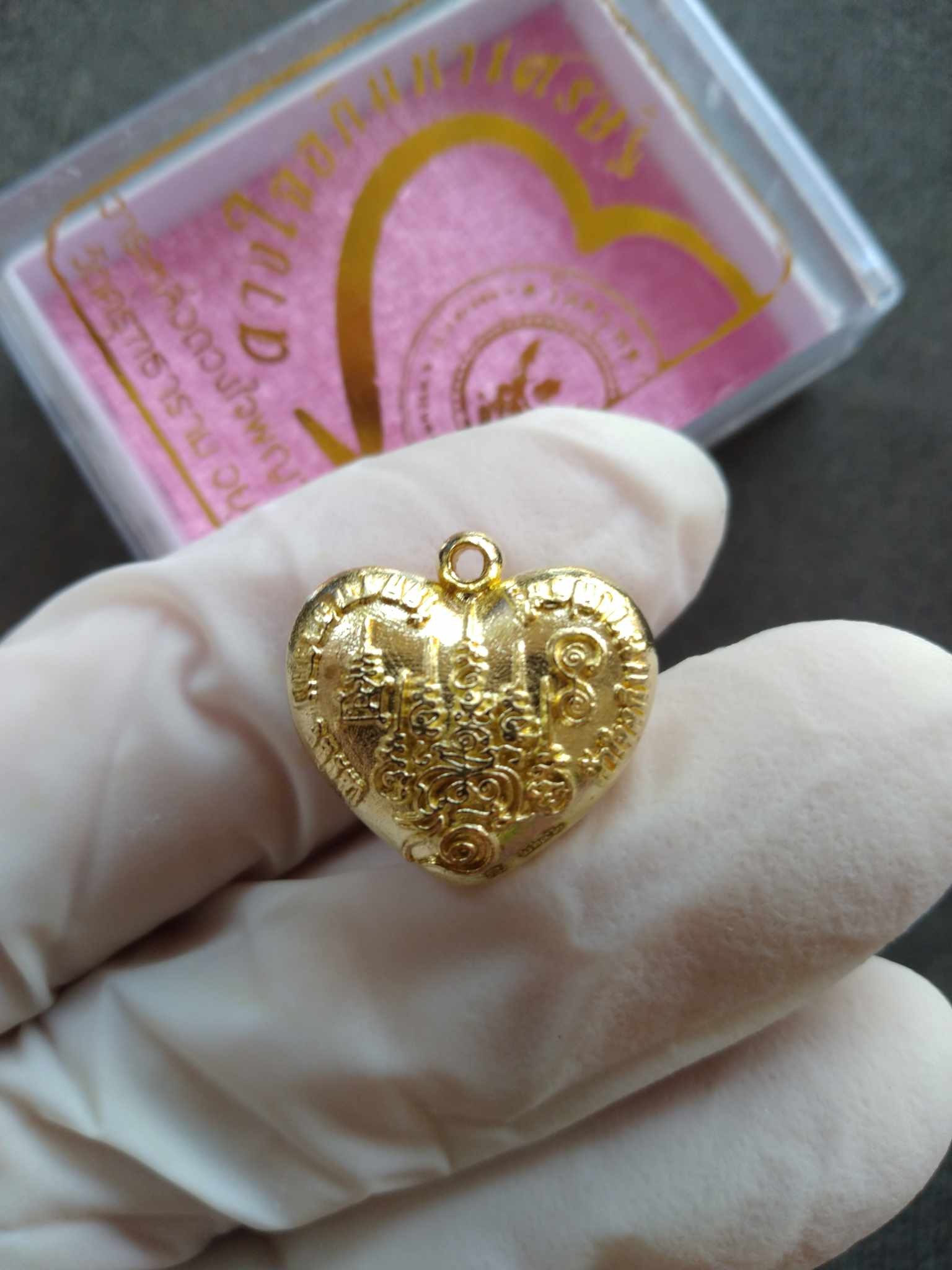 Garuda heart amulet gold heart pendant with intricate Garuda engraving held in gloved hand