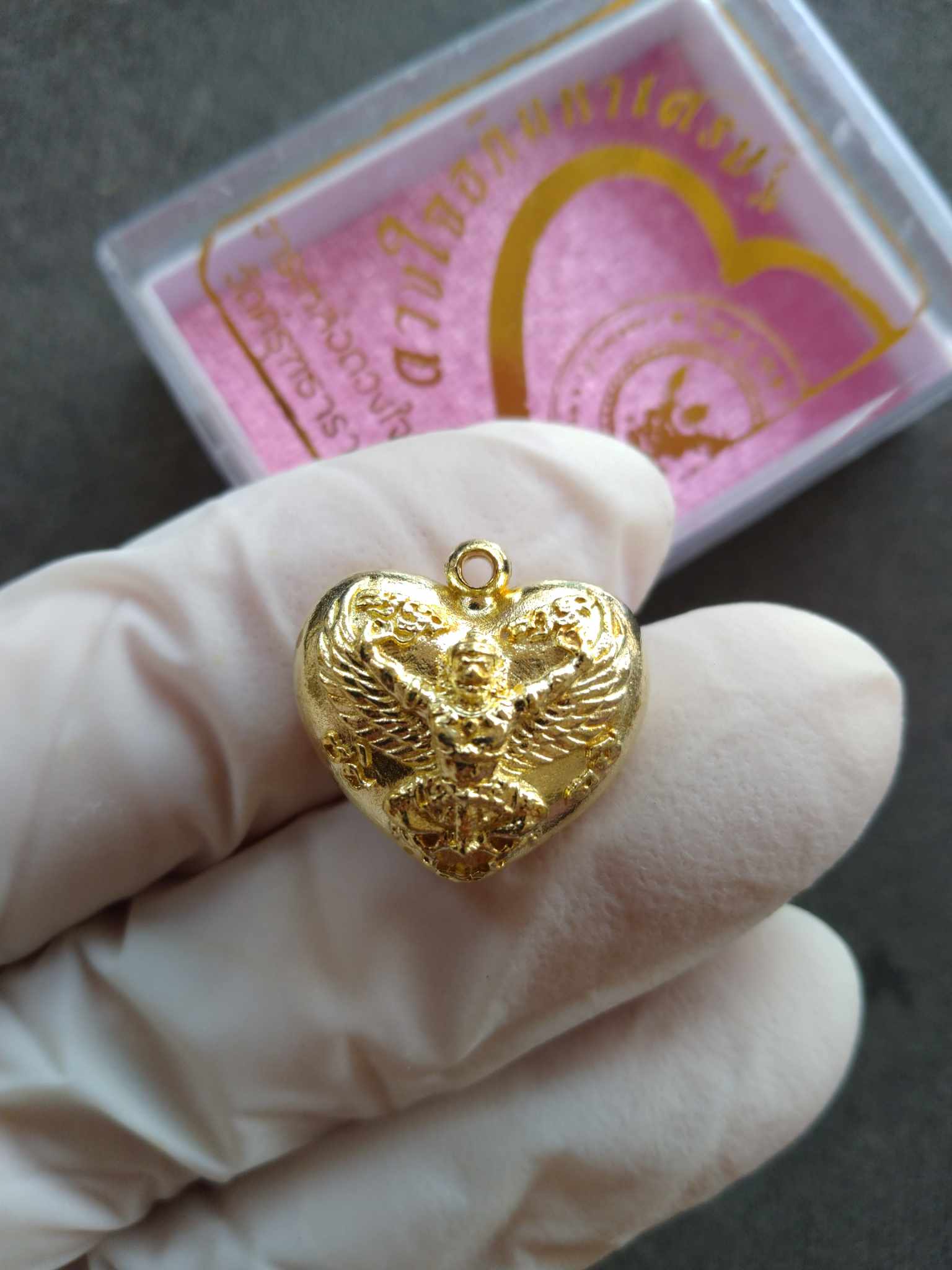 Thai Blessing Co Garuda heart amulet gold heart pendant held in gloved hand with pink gift box