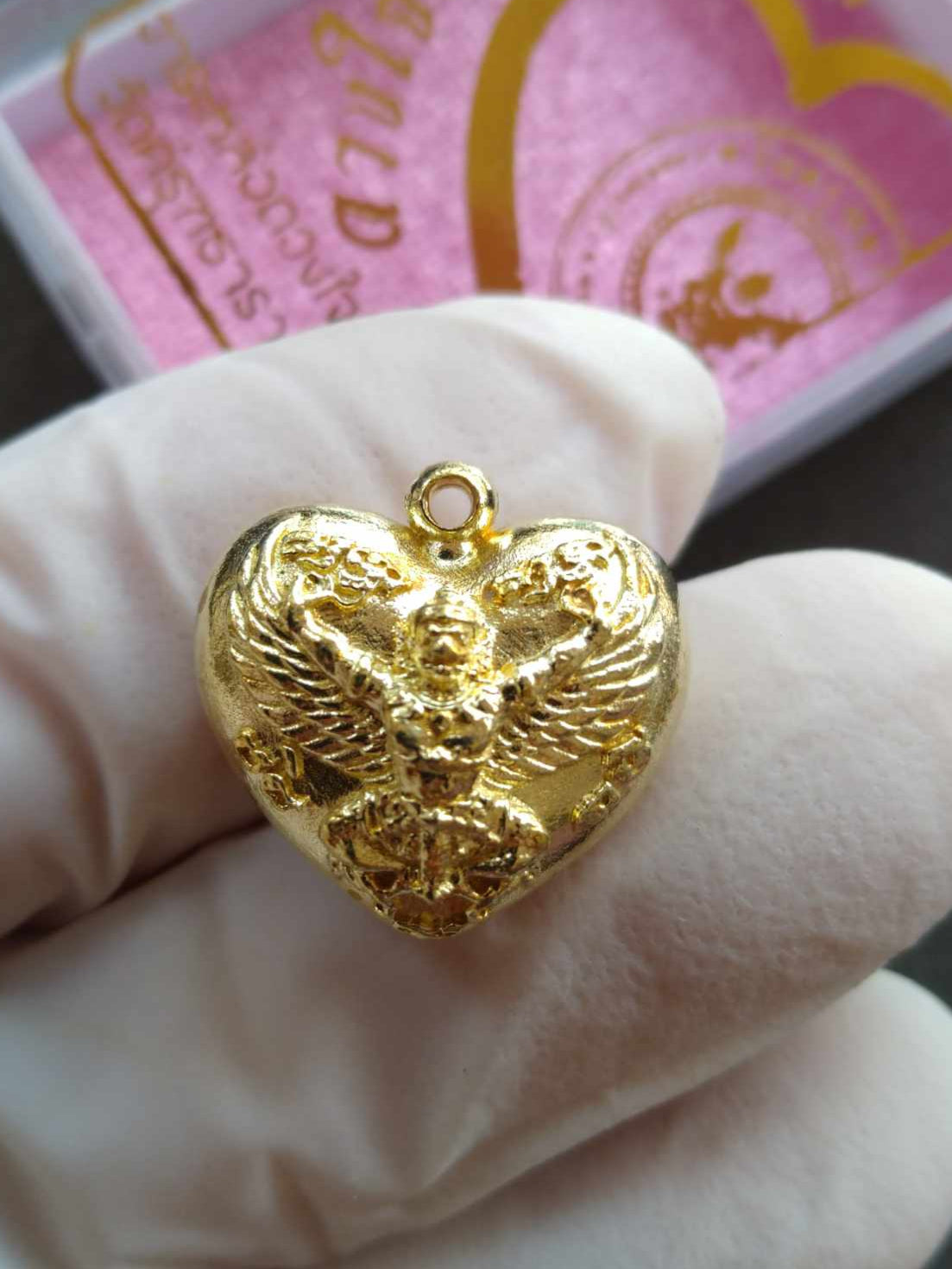 Garuda heart amulet gold heart shaped pendant with detailed Garuda relief held in white glove
