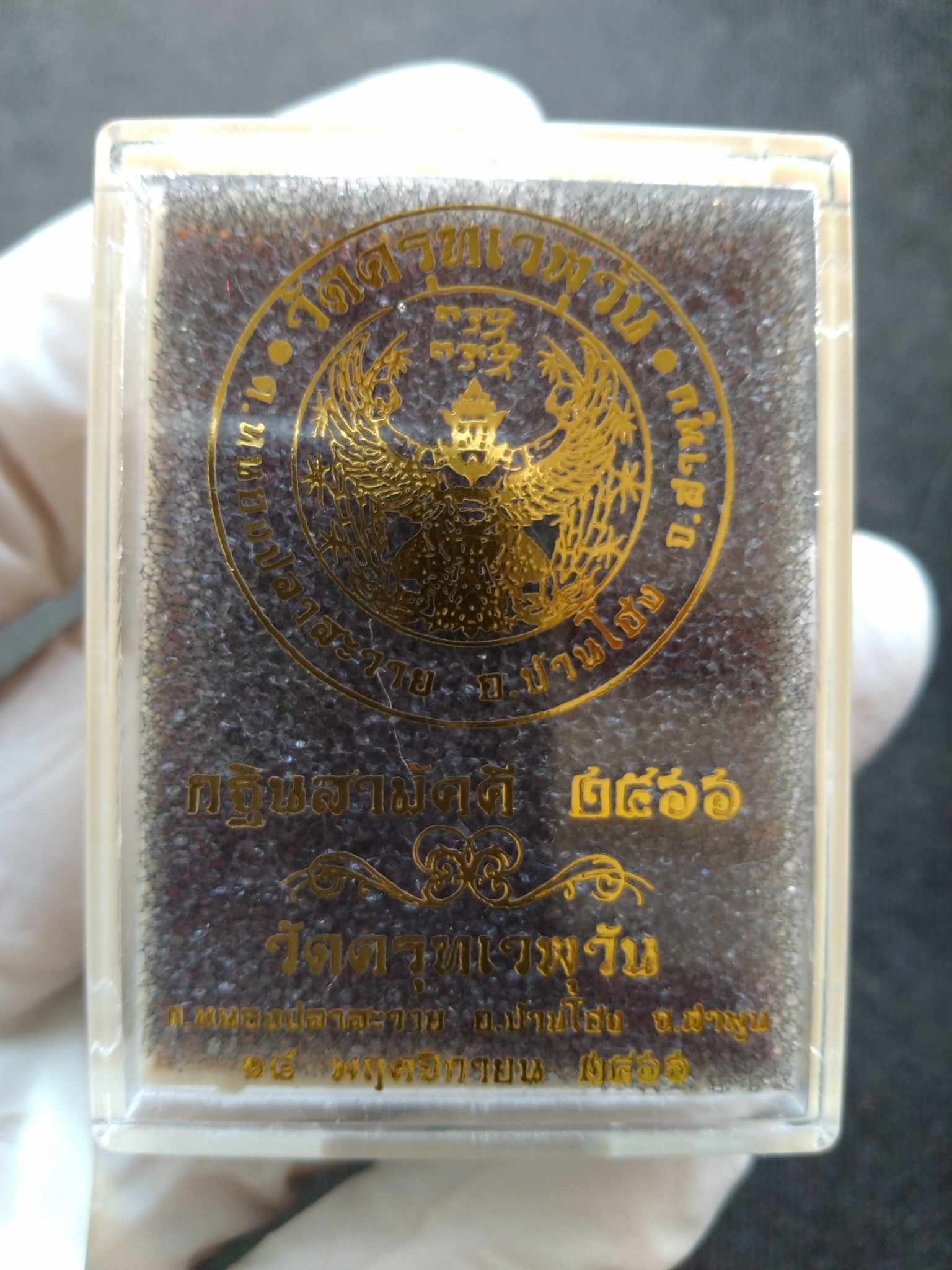 Garuda Phaya Krut Noi amulet in clear plastic display box with gold Garuda emblem on brown cushion