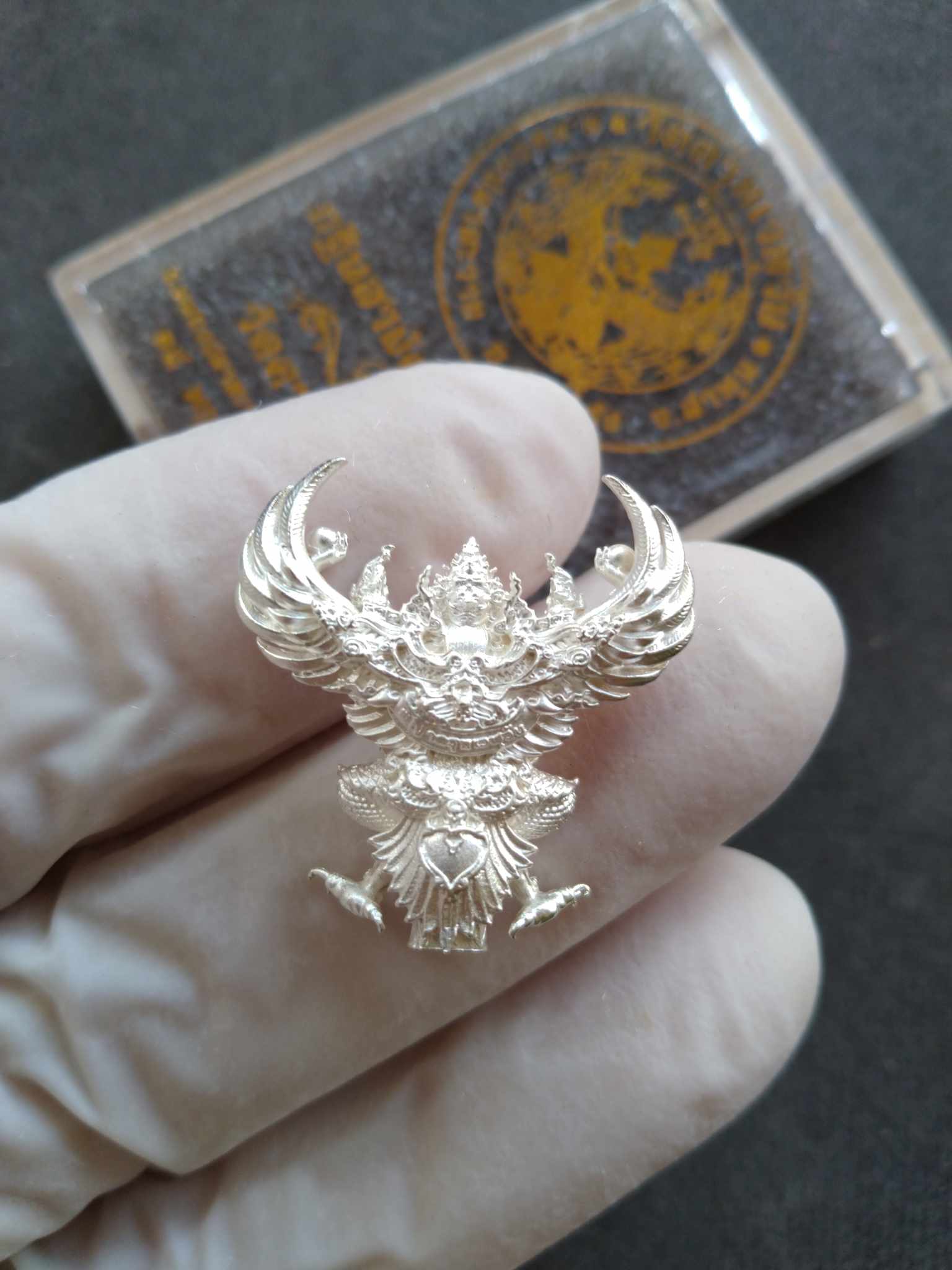 Garuda Phaya Krut Noi amulet silver pendant held by gloved hand showing intricate Thai Blessing Co design