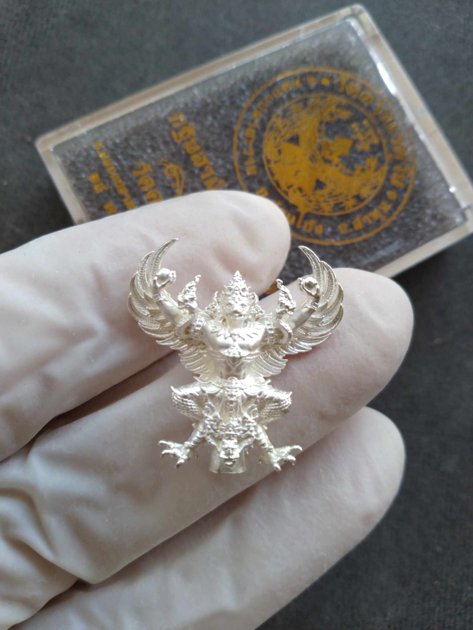 Garuda Phaya Krut Noi amulet intricate silver pendant held in gloved hand with clear Thai Blessing Co case