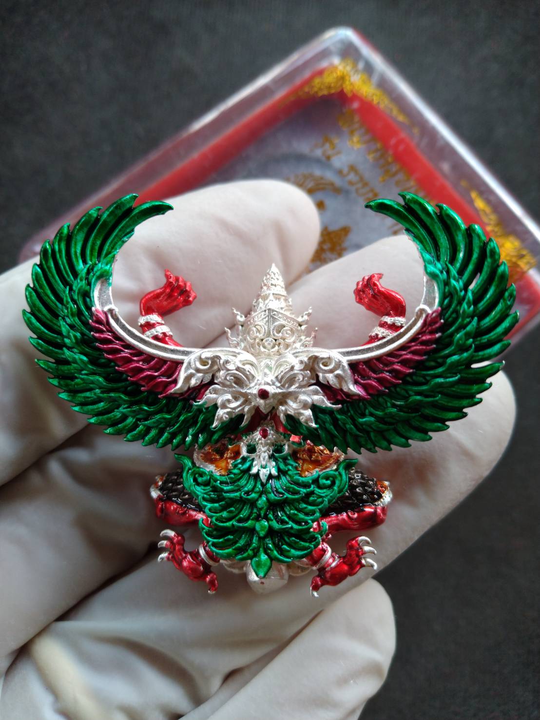 Garuda Wealthy Millionaire Edition Thai amulet pendant, green enamel wings red accents silver details held in gloved hand