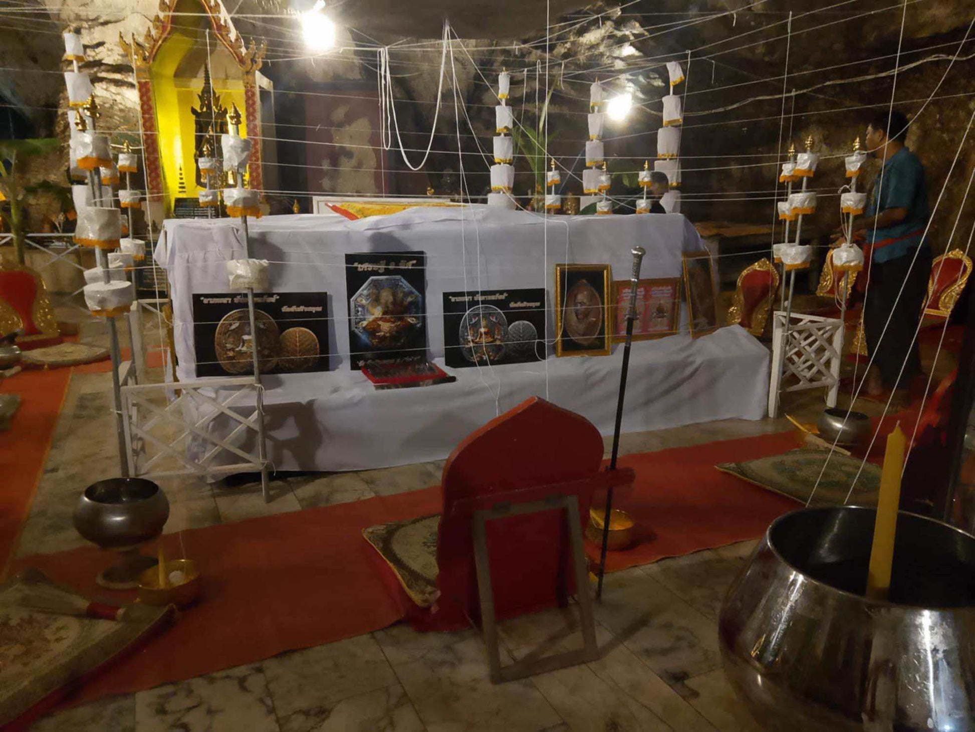 Hoon payon sacred puppet for protection on a temple altar with white cords candles offering bowls and chairs