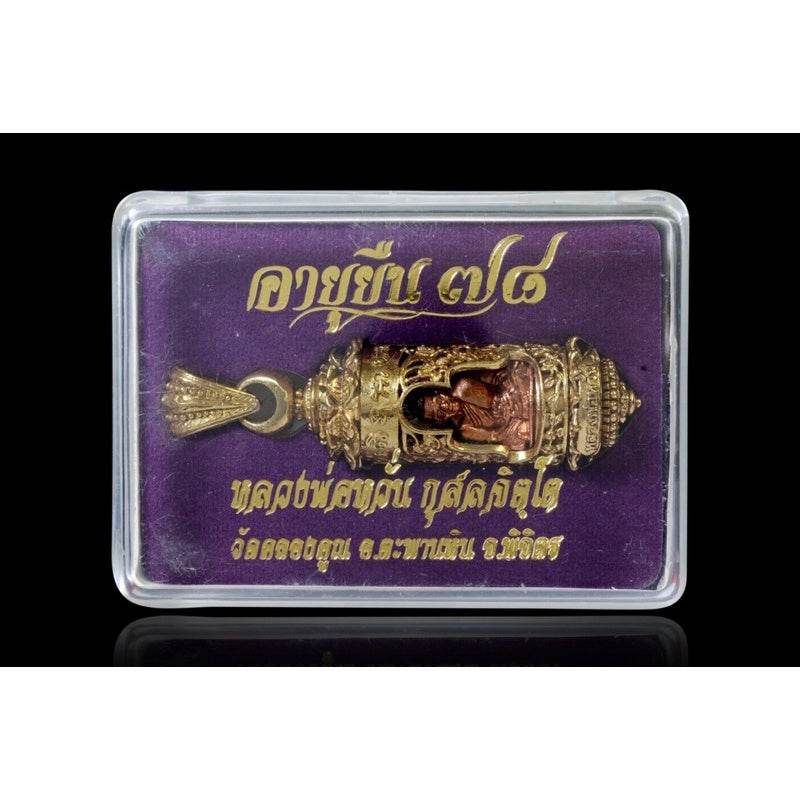 Khun Setthi Takrud longevity amulet in ornate gold casing displayed in clear plastic box on purple velvet