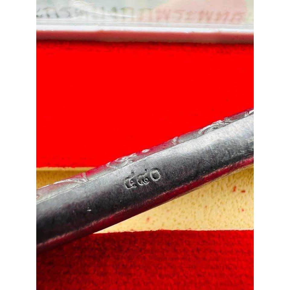 Close up silver lead takrut blessed by Luang Pu Paew showing stamped metal tube on red velvet pouch