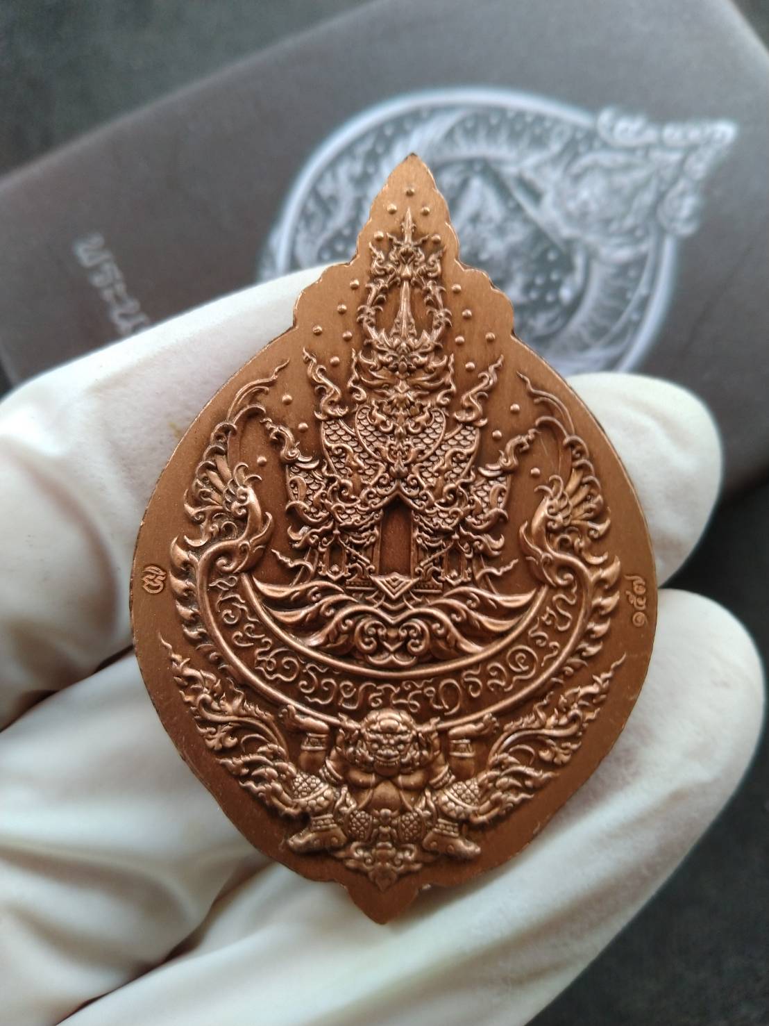 Lord Narai on Garuda amulet copper pendant with intricate Thai embossed design held in gloved hand