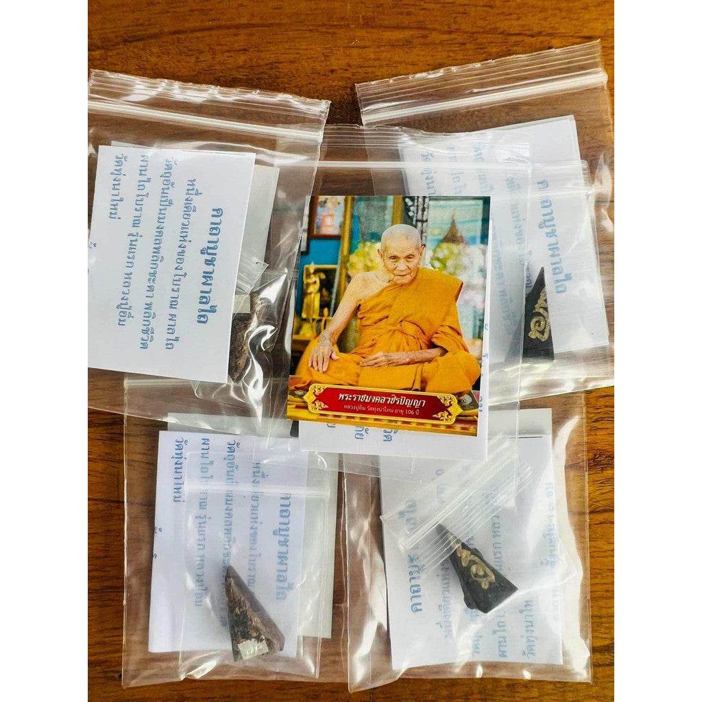 Luang Pu Im ploughshare amulet sealed in small plastic bags displayed with a monk photo card