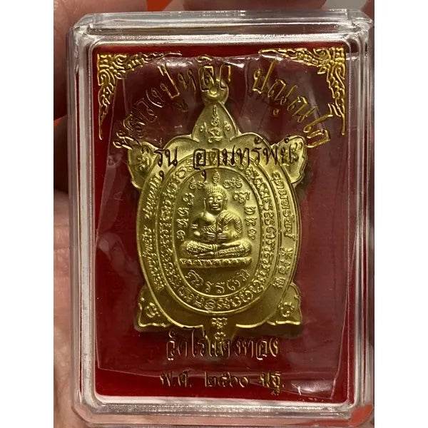 Gold Luang Pu Liew turtle amulet in clear plastic case with red backing showing seated Buddha figure