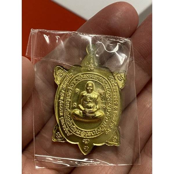 Thai Blessing Co Luang Pu Liew turtle amulet gold metal talisman in clear plastic pouch held in hand