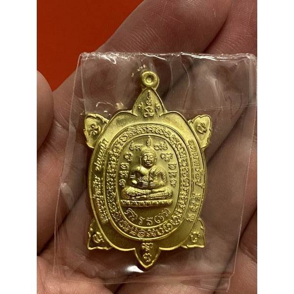 Handheld gold Luang Pu Liew turtle amulet in plastic bag showing seated monk and Thai script
