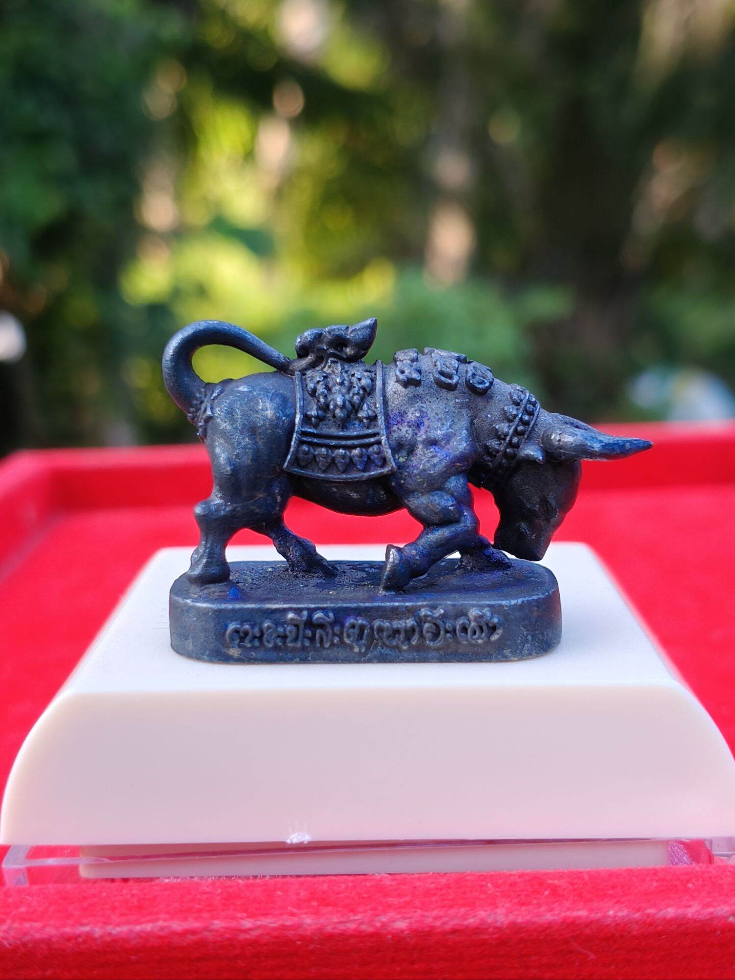 Luang Pu Lun buffalo charm for luck bronze amulet on white display base with Thai inscription and ornate saddle