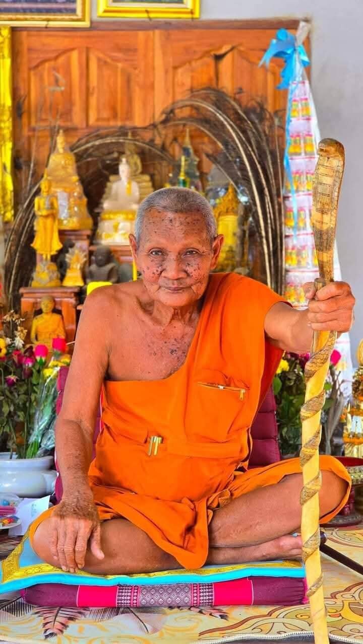 Luang Pu Lun buffalo charm for luck shown with Thai monk in orange robe blessing the amulet at shrine