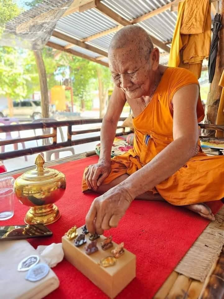 Elder Thai monk arranging small amulets on red cloth including Luang Pu Lun buffalo charm for luck at shrine