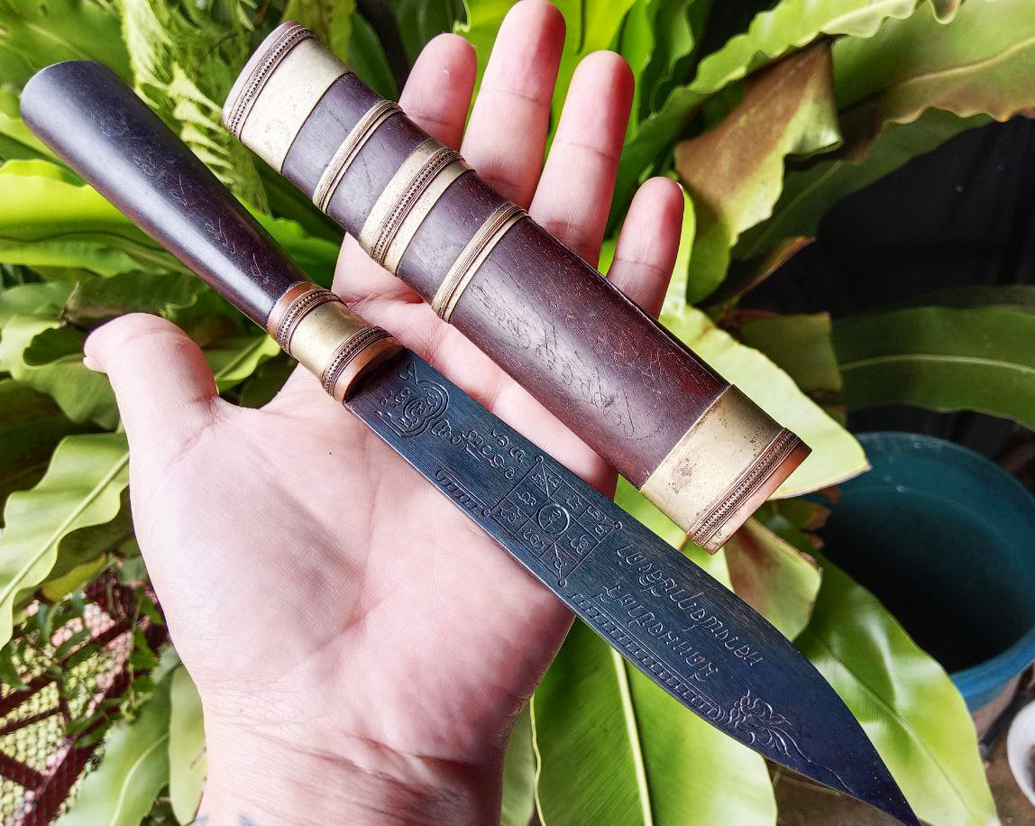 Hand holding Luang Pu Moon ritual knife with engraved blade and wooden handle and matching sheath