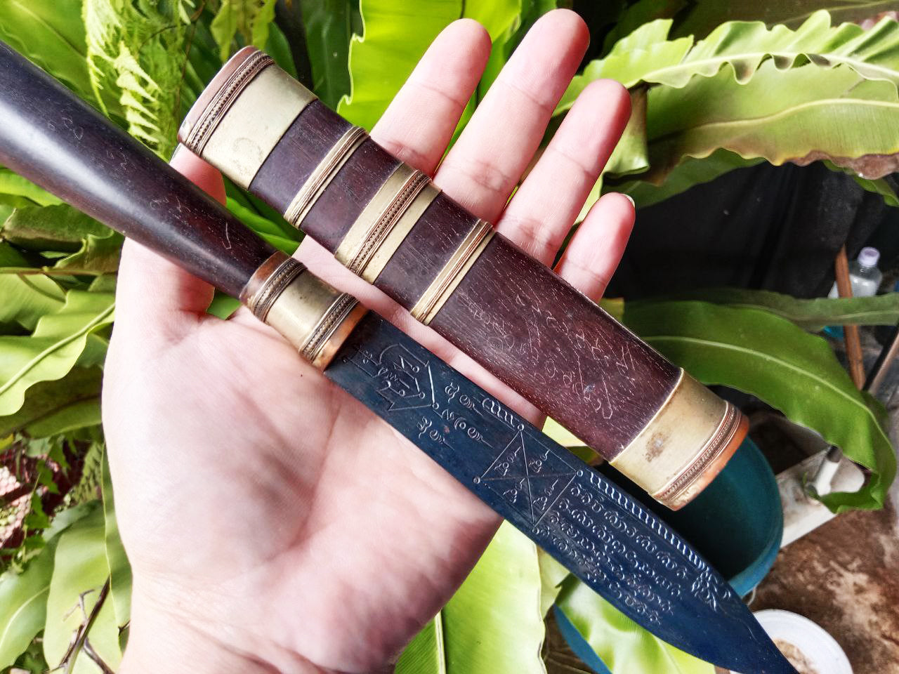 Hand holding Luang Pu Moon ritual knife with engraved dark blade and wooden sheath with brass fittings