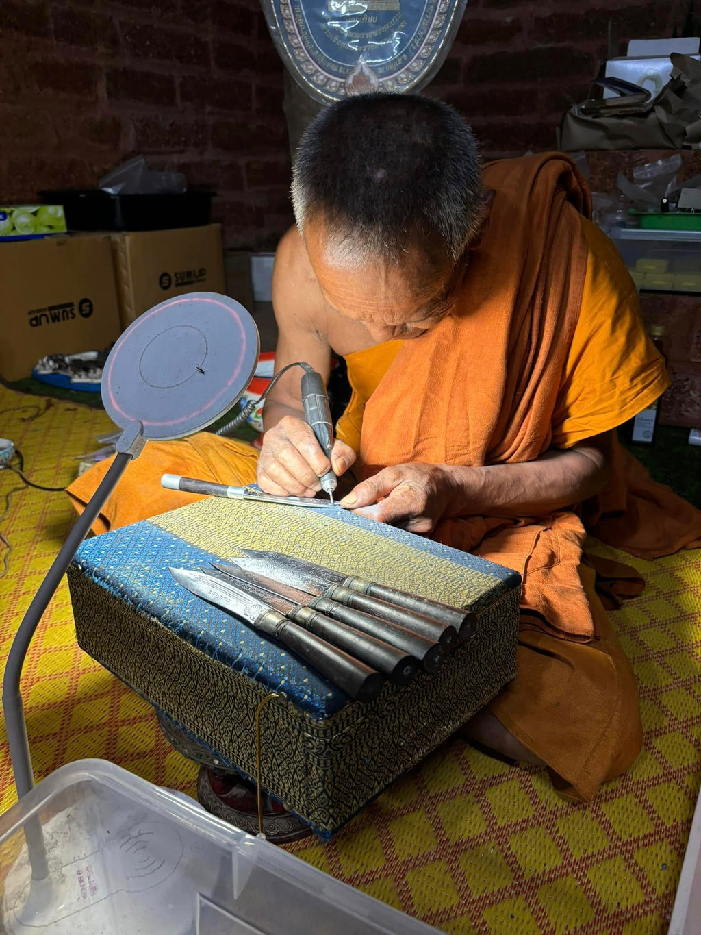 Thai monk crafting Luang Pu Moon ritual knife on cushion with metal blades and carving tools