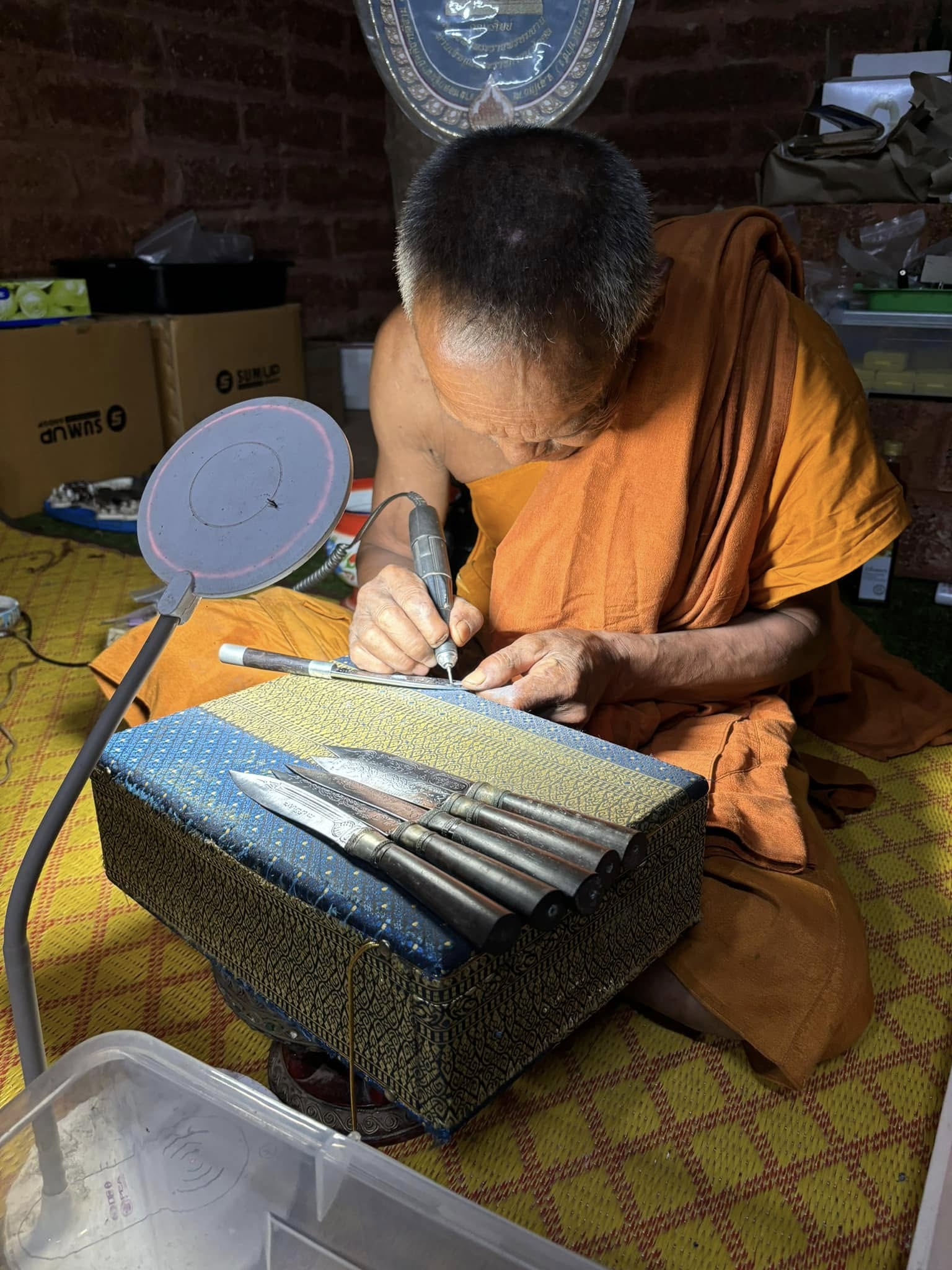 Thai monk crafting Luang Pu Moon ritual knife on cushion with metal blades and carving tools