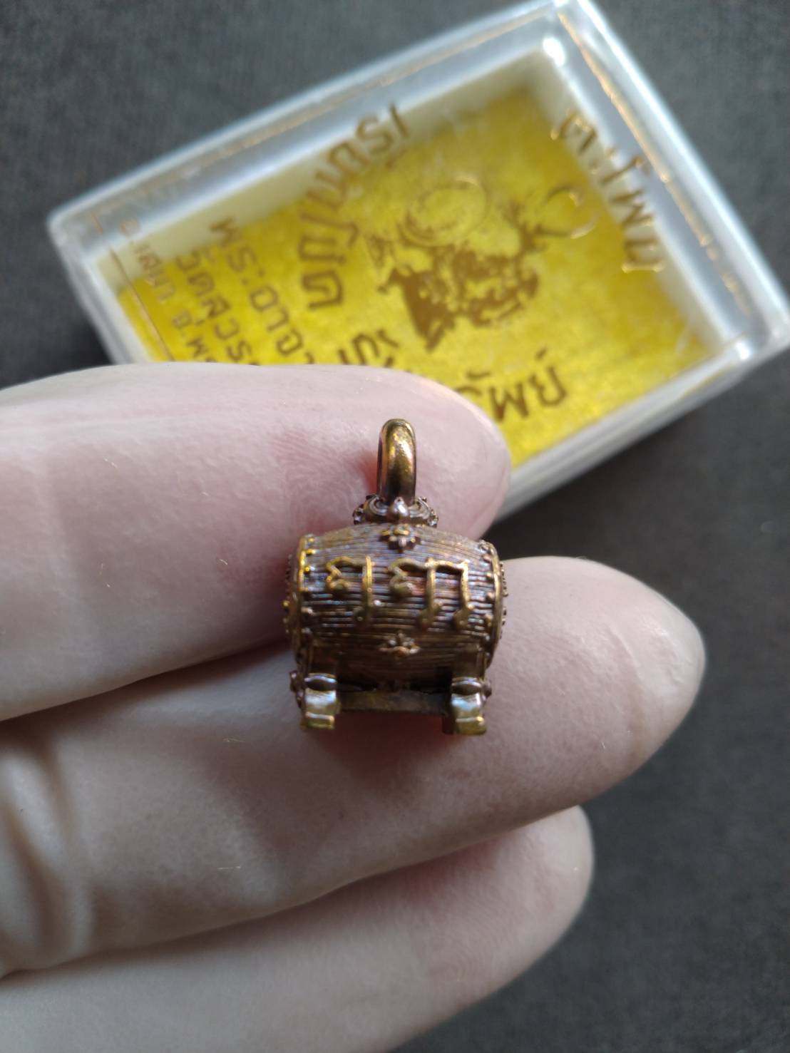 Thai Blessing Co small gold barrel pendant Lucky amulet charm held between fingers with plastic case