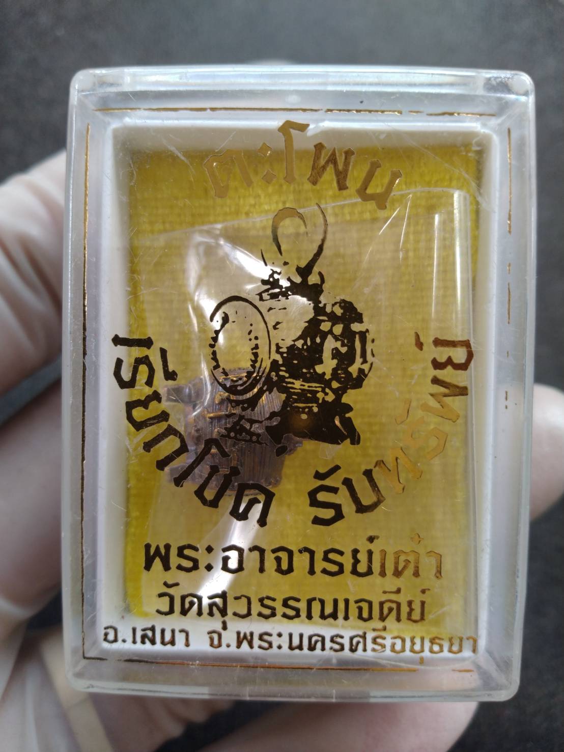 Thai metal Buddha pendant in clear plastic display case with yellow backing and Thai script Lucky amulet