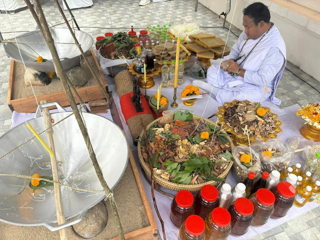 Thai Blessing Co priest in white robes performing Luuk Sawat sacred charm blessing with herbs jars marigolds