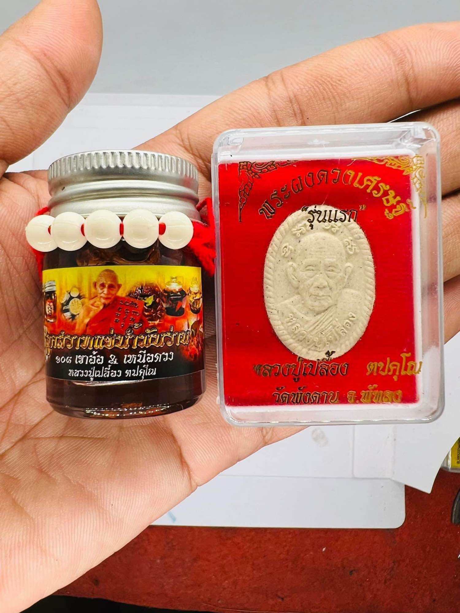 Luuk Sawat sacred charm set with monk amulet in plastic case and small jar with white lucky beads held in hand