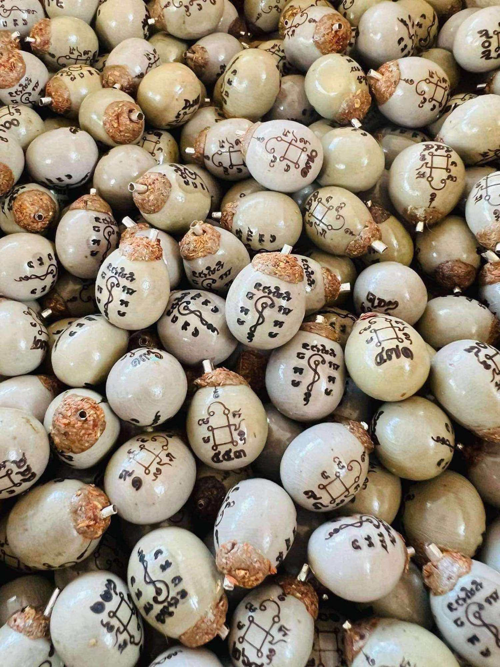 Thai Blessing Co Luuk Sawat sacred charm pile of beige white talisman seeds with hand drawn black yantra script
