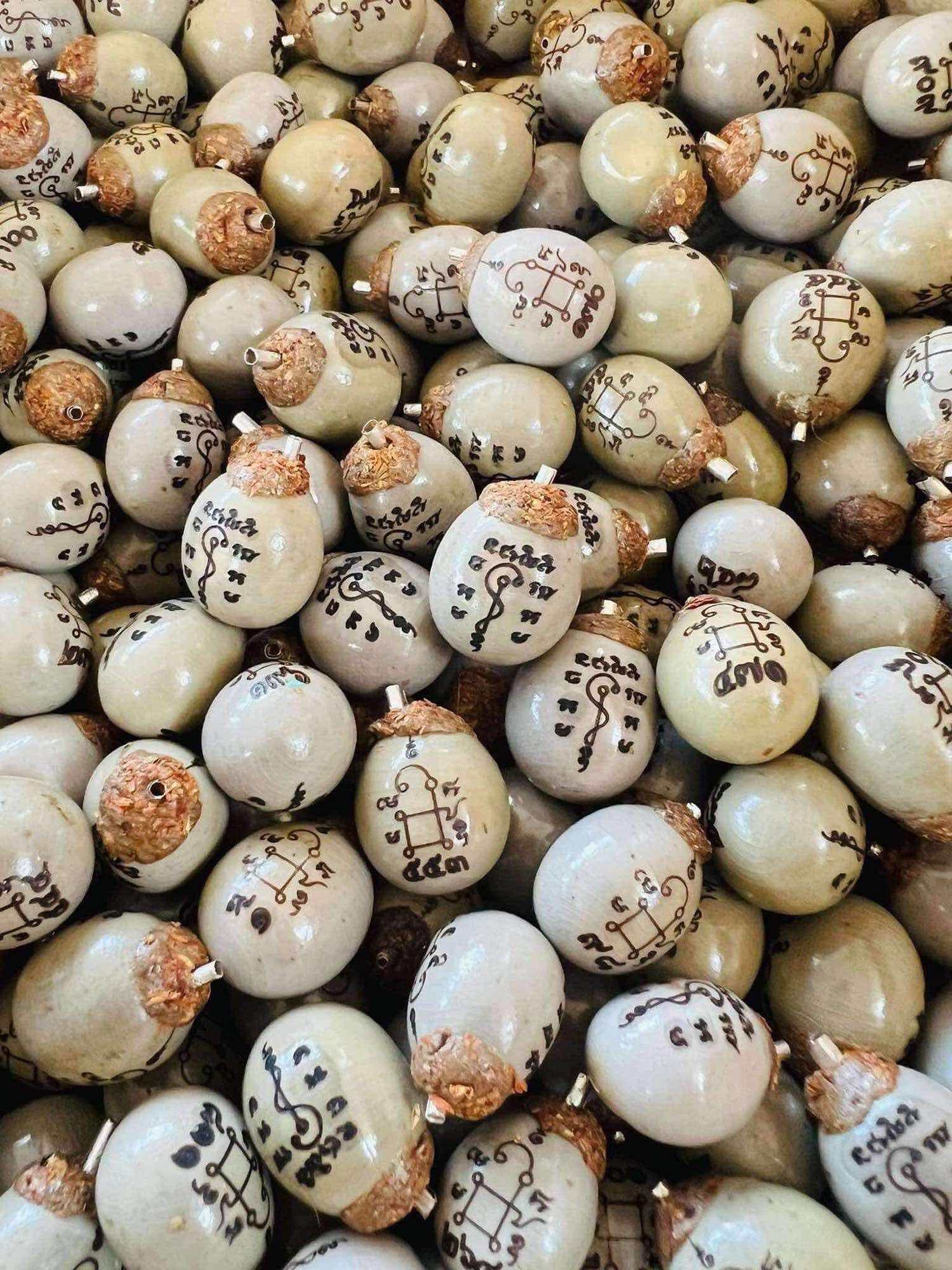 Thai Blessing Co Luuk Sawat sacred charm pile of beige white talisman seeds with hand drawn black yantra script