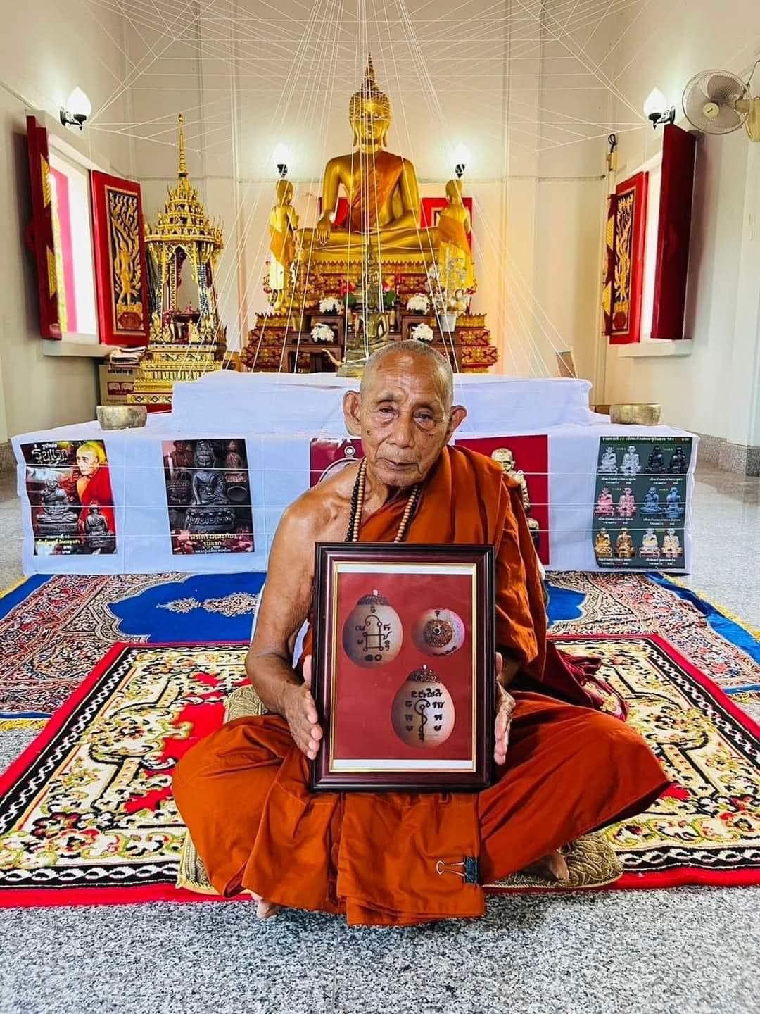 Monk in temple holding framed Luuk Sawat sacred charm amulets with golden Buddha altar background