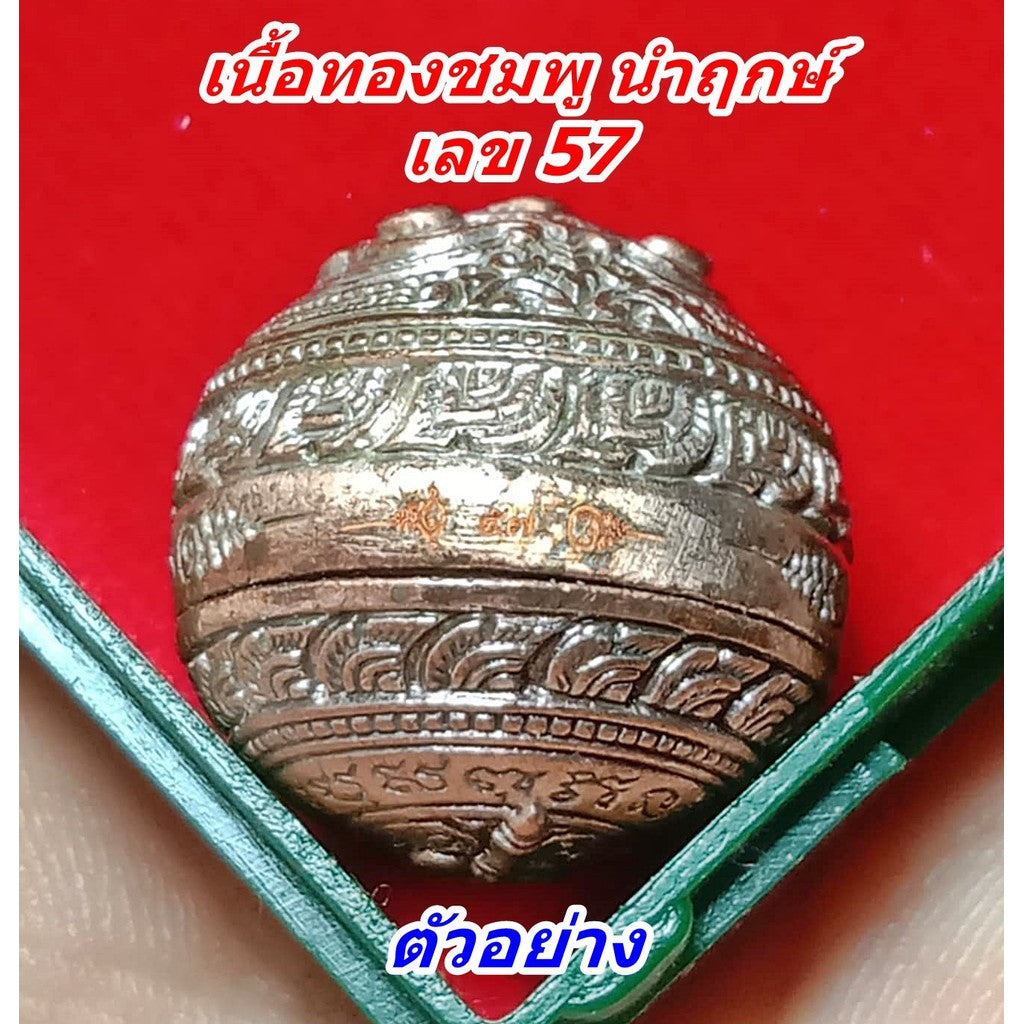 Close up engraved copper ball amulet with Thai script in green case on red background Mercury Hor Twin Rahu amulet for wealth