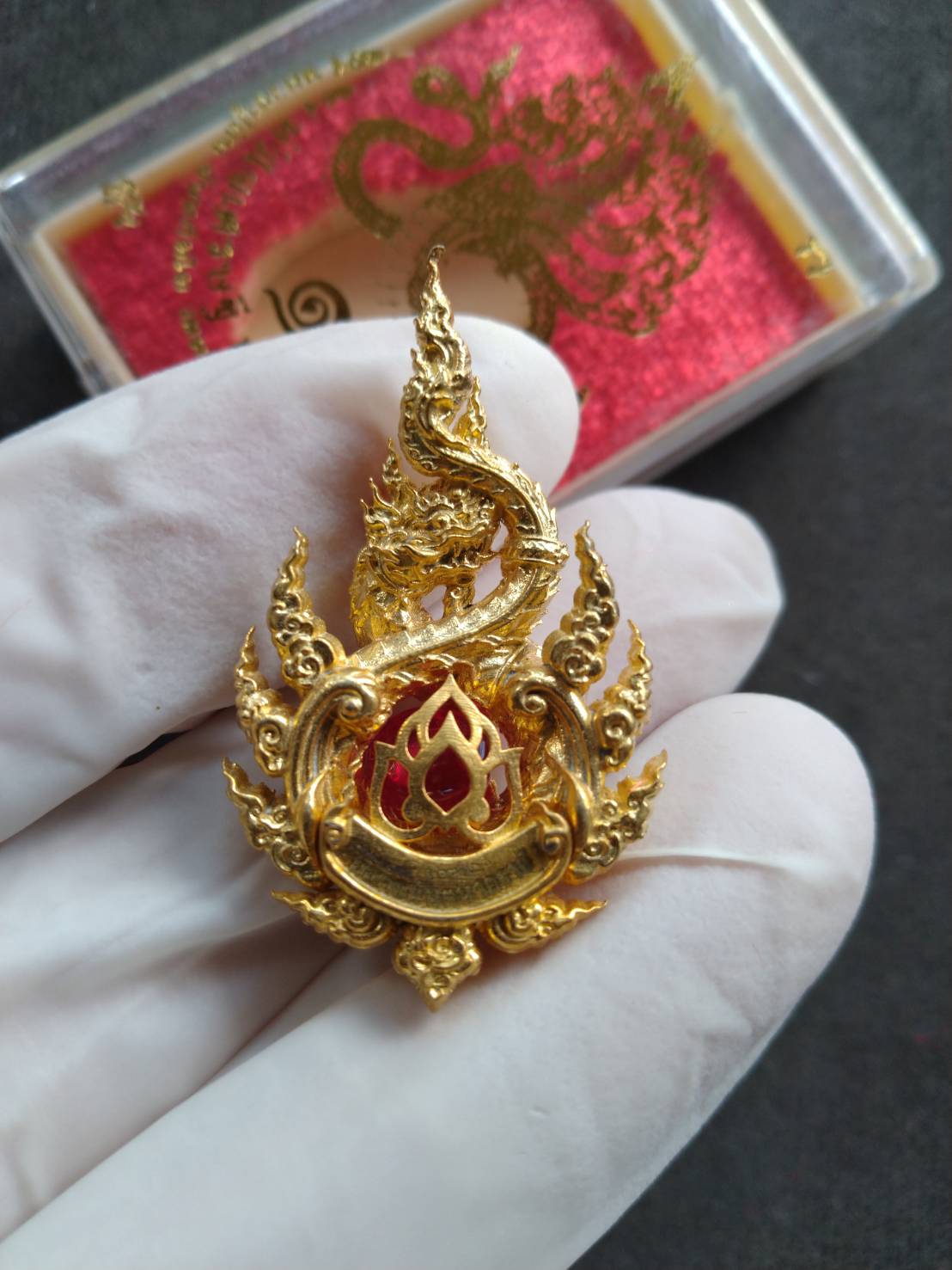Naga King Ananta pendant gold ornate Thai Buddhist naga with red enamel center held in gloved hand