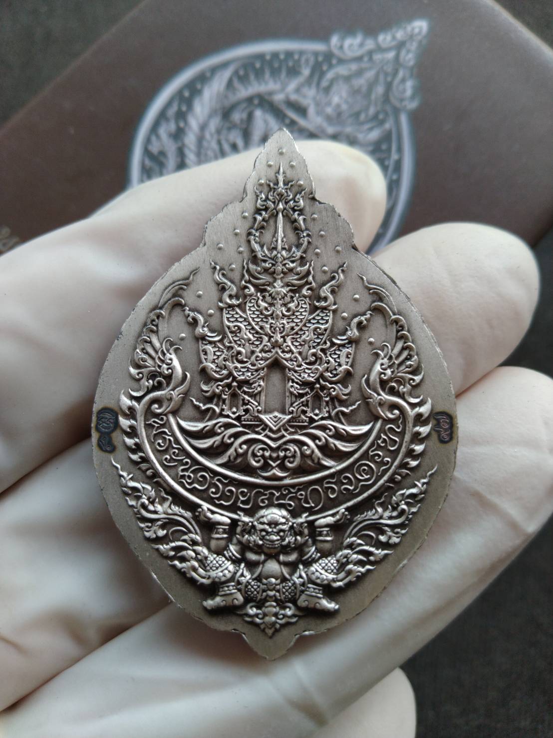Narayana on Garuda silver amulet held in gloved hand showing intricate Thai deity and mythical bird motifs