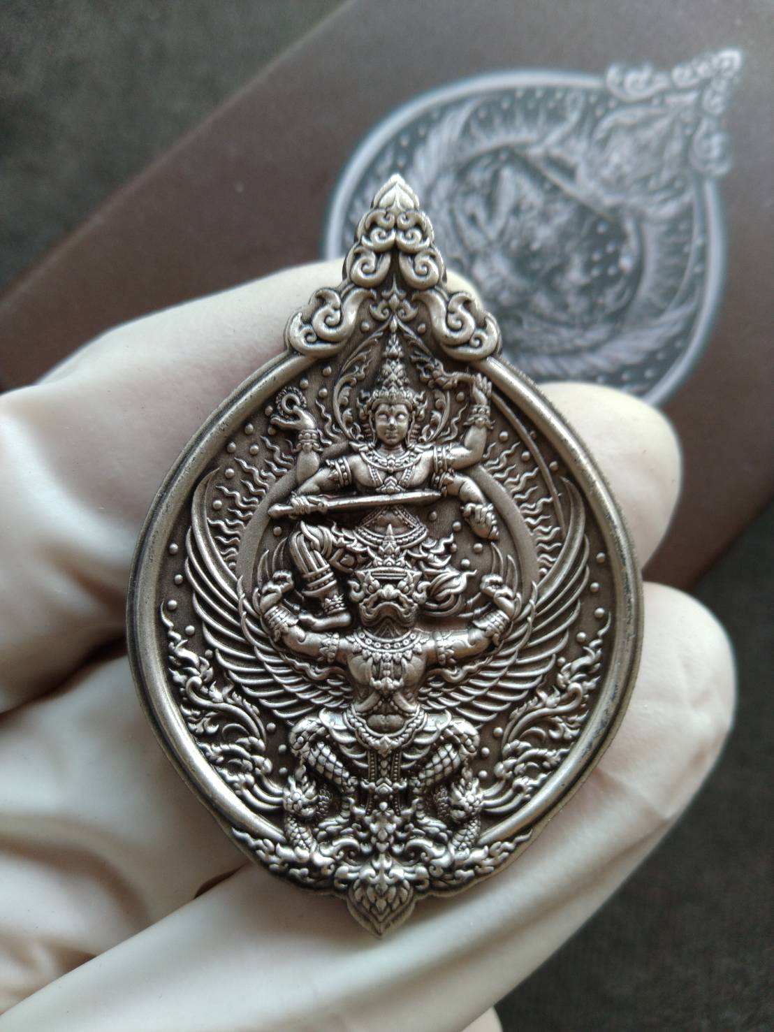 Narayana on Garuda silver amulet ornate teardrop Thai Blessing Co pendant shown in gloved hand