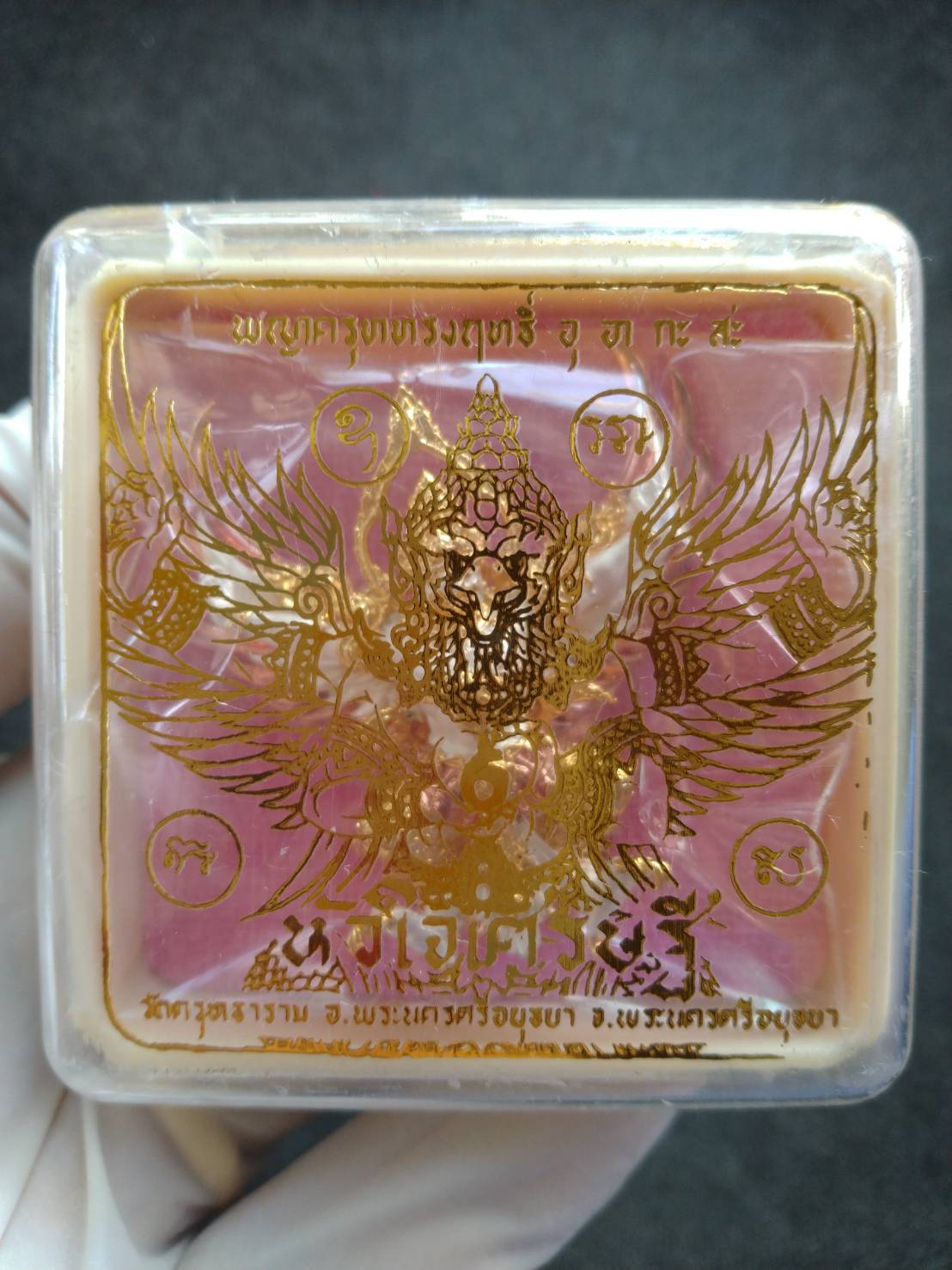 Phaya Garuda amulet for wealth in clear plastic case with pink base gold Garuda design and Thai script