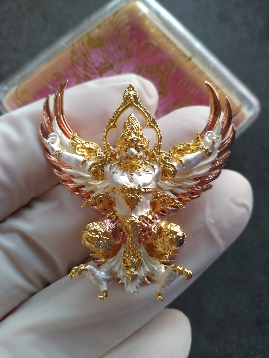 Thai Blessing Co gold white and copper Phaya Garuda amulet for wealth pendant with intricate filigree held in gloved hand