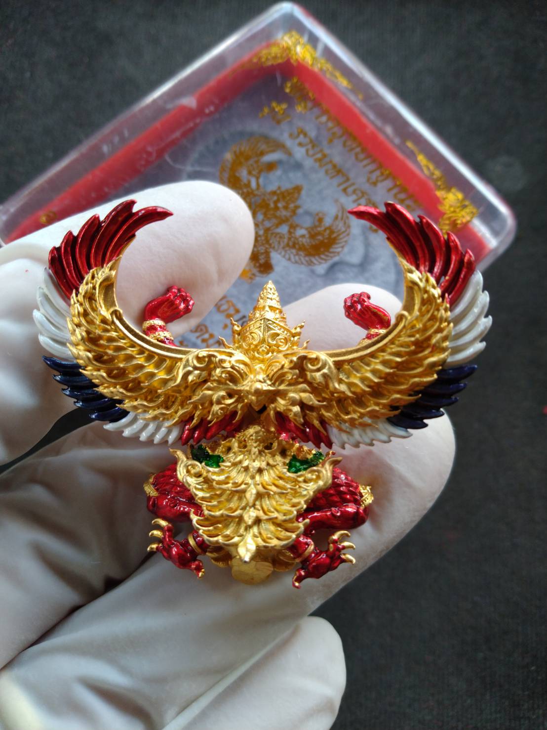 Phaya Garuda amulet for wealth gold red multicolor Garuda pendant held in gloved hand with display case