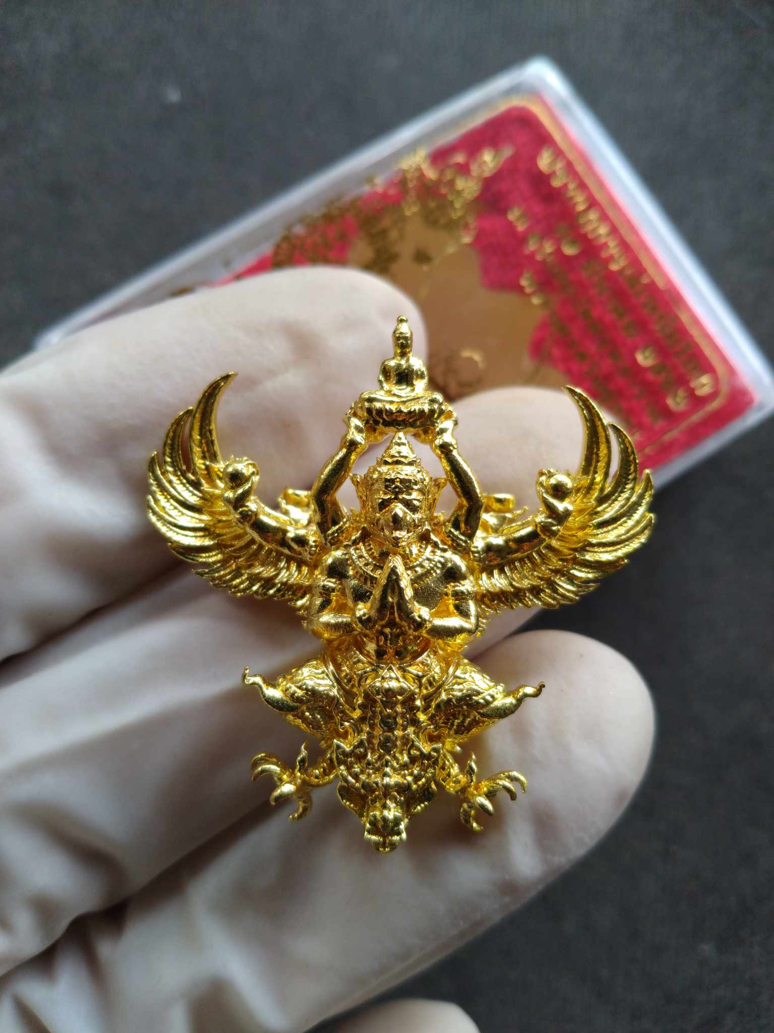 Gold Phaya Garuda royal amulet pendant sacred talisman with detailed wings held in gloved hand by Thai Blessing Co