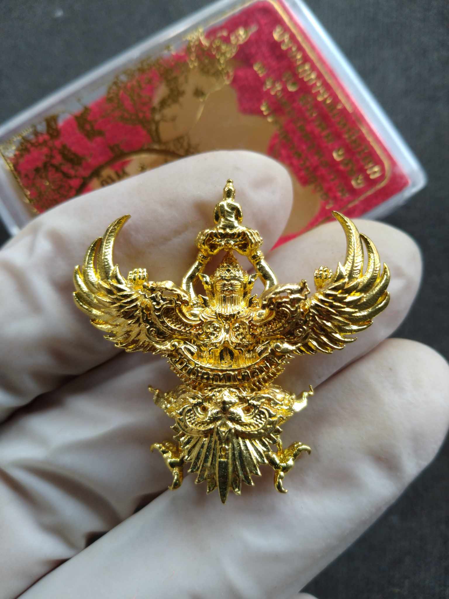 Phaya Garuda royal amulet gold pendant held in gloved hand showing detailed wings and face