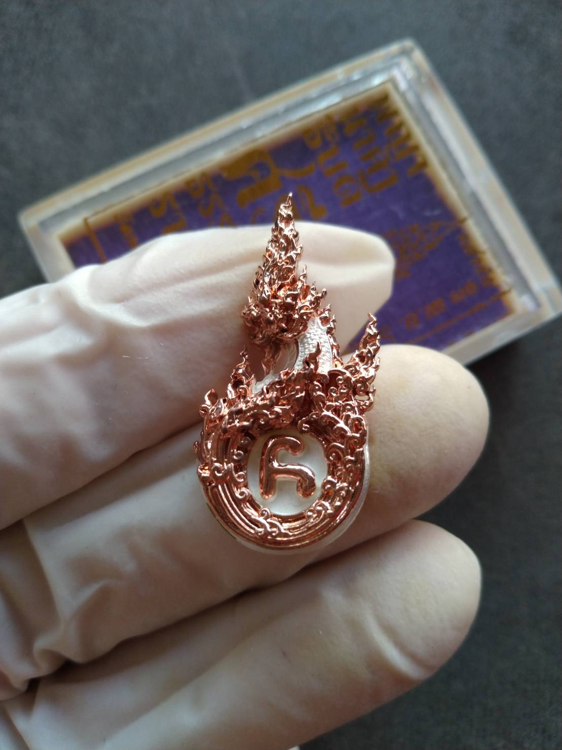 Phaya Naga amulet for prosperity copper flame shaped Thai pendant with intricate naga design held in gloved hand