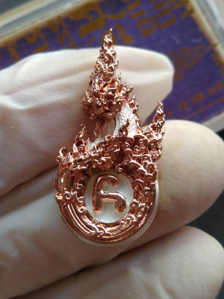 Phaya Naga amulet for prosperity rose gold metal pendant with intricate flame and Naga design held by gloved fingers