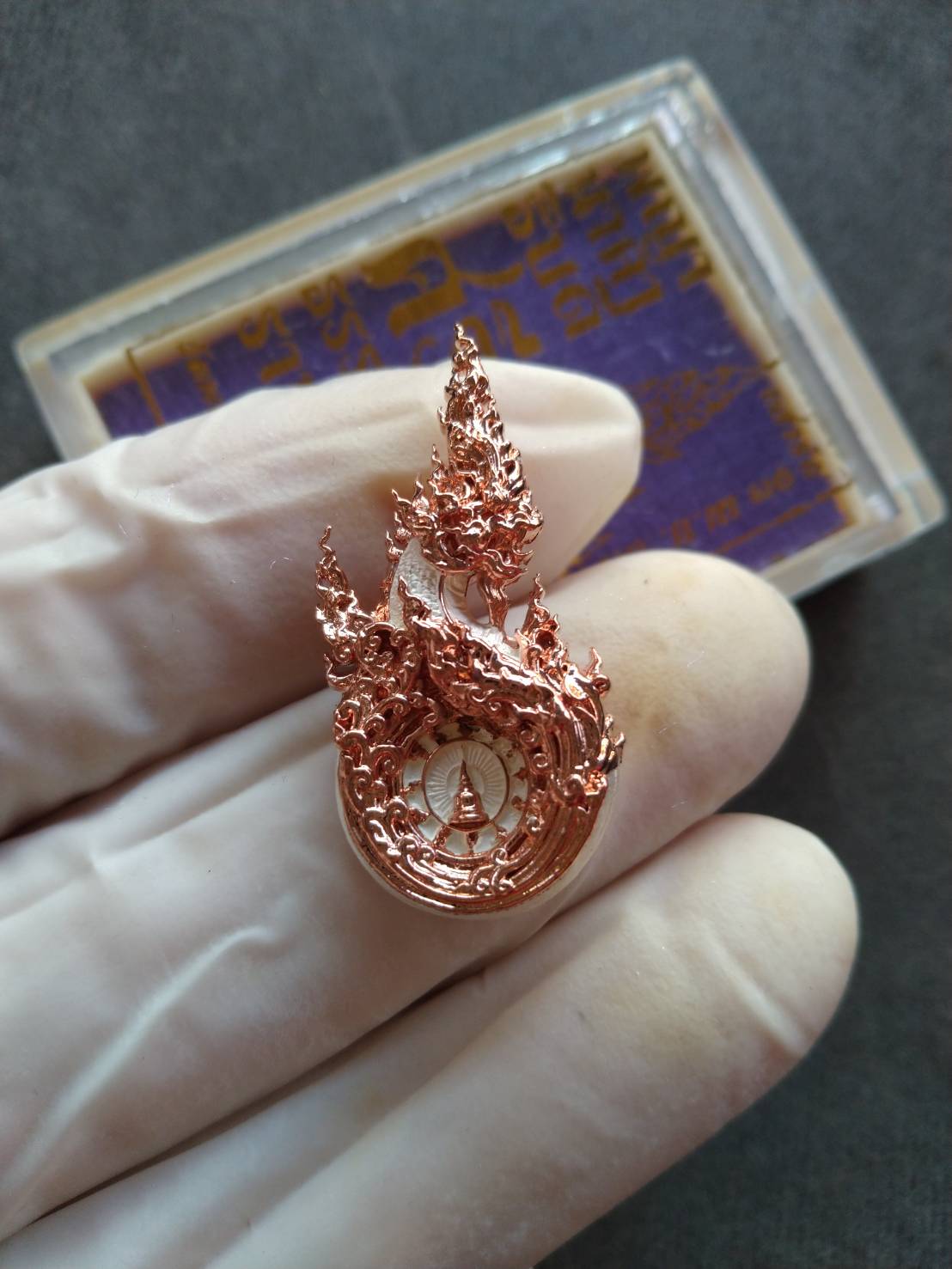 Phaya Naga amulet for prosperity copper pendant with intricate flame Naga design held in gloved hand