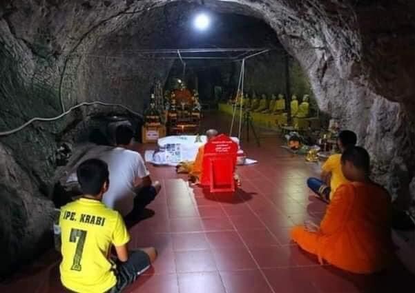 Phaya Tao Reuan amulet for wealth displayed at cave shrine with monks and worshippers around altar